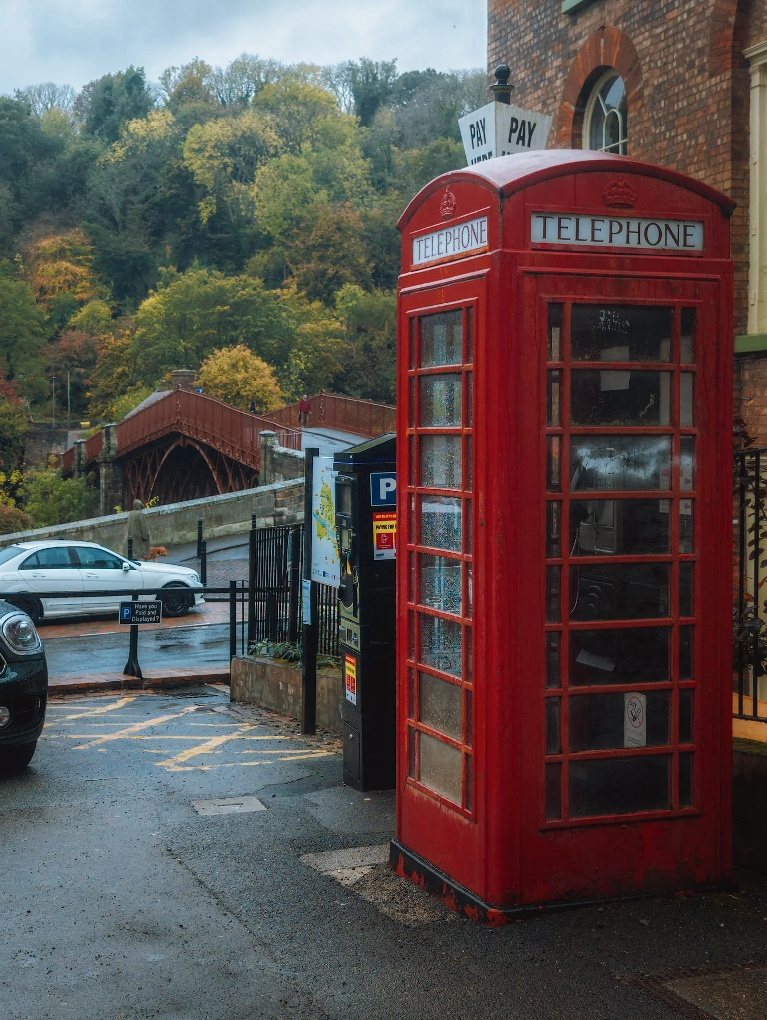 A quintessentially British red telephone box, mirroring the red of the Iron Bridge in the distance.