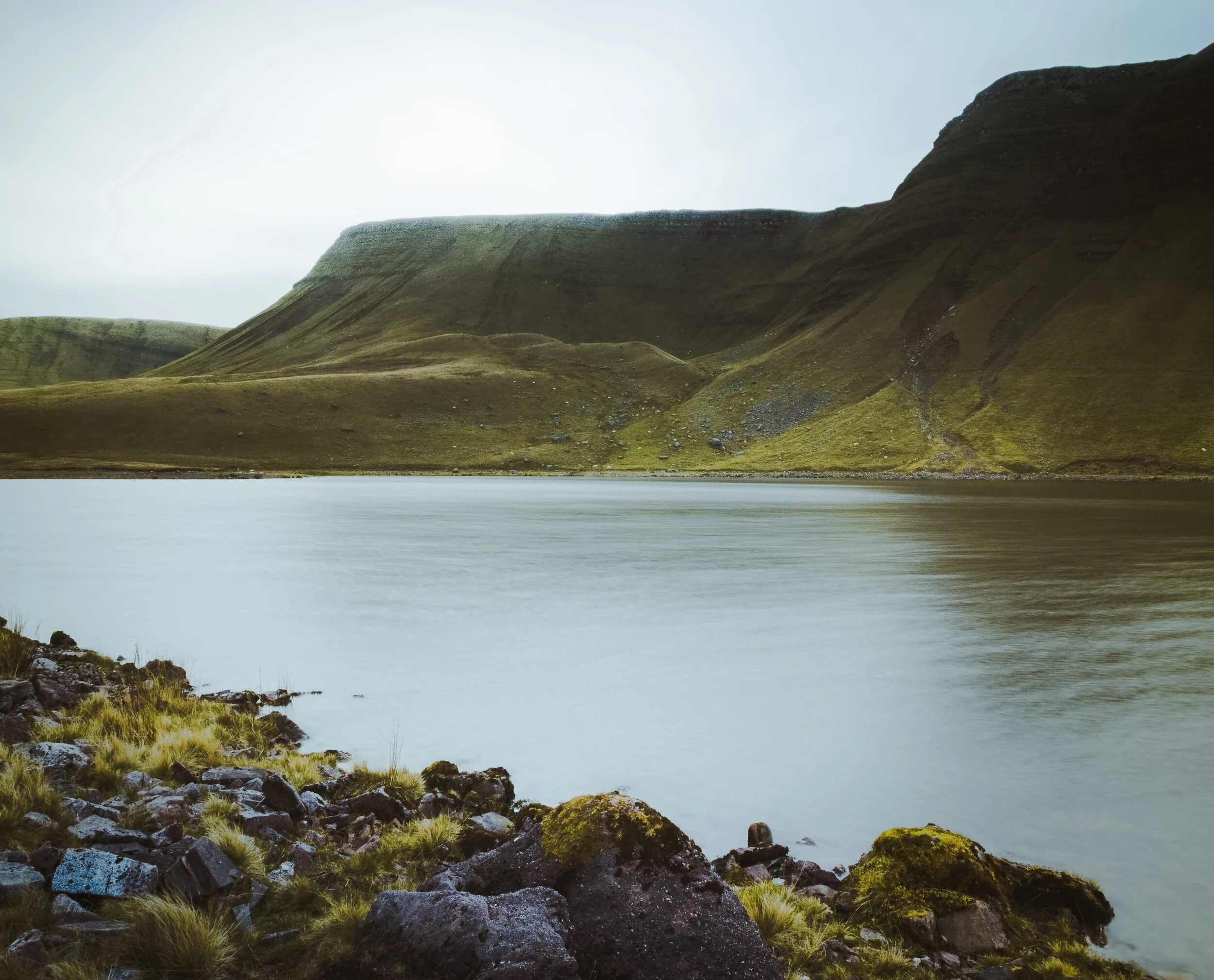 An overcast long exposure at Llyn y Fan Fach with two of the sloping peaks of the Carmarthen Fans.