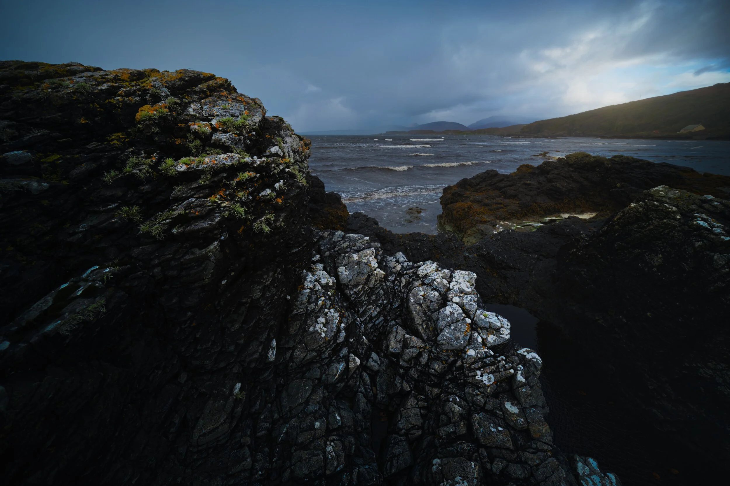 A hint of the Black Cuillins in the distance as a break in the thick cloud cover allows some dramatic spotlighting.